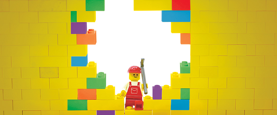 Image of a lego man knocking down a wall made of legos